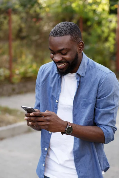 Happy man using mobile phone apps, texting message, browsing internet, looking at smartphone. Handsome Afro-American man using smartphone and smiling. Young people working with mobile devices