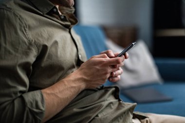 Akıllı telefonu tutan eller. Cep telefonu uygulamaları, mesaj gönderme, internette gezinme, evde oturma portresi. Mobil aygıtlarla çalışan gençler