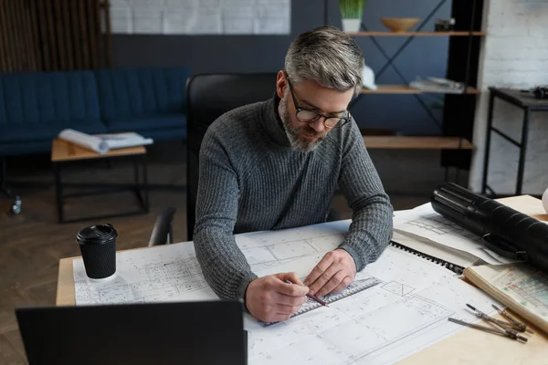 Diseñador de interiores que trabaja en la oficina con planos. Ingeniero inspeccionar plan arquitectónico, bosquejando un proyecto de construcción. Retrato de hombre barbudo guapo en el lugar de trabajo. Concepto de construcción empresarial — Foto de Stock