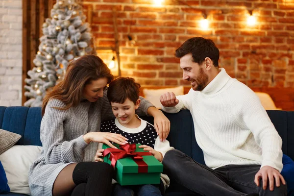 Anne babalar sevimli oğluna hediye paketi sunuyor. Noel çocukları, çocuk, portre. Mutlu bir aile Noel sabahı birlikte geçirir. Kış tatilleri, Noel kutlamaları, yeni yıl konsepti.