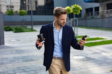 Akıllı telefon kullanan ve gülümseyen yakışıklı bir iş adamı. Mutlu genç adam cep telefonu uygulamaları kullanıyor, mesaj atıyor, internette geziniyor, akıllı telefona bakıyor. Mobil aygıtlarla çalışan gençler