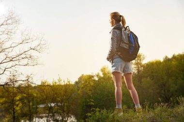 Geri nehir ve mavi gökyüzü karşı uçurumdaki erken sabah saat ayakta bir kız backpacker görüntülemek