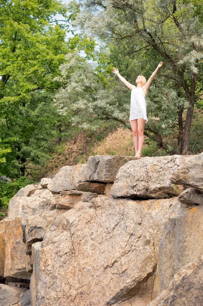 若い女の子は 空まで両手で崖の端に天気の良い日を楽しんでいます 美しい短い白いドレスを着た女性 — ストック写真