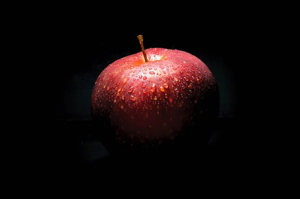 fresh red apple with droplets of water against black background with space for text