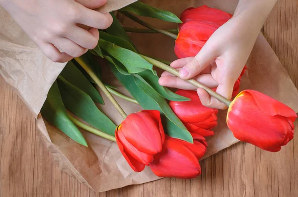 beautiful bouquet of red tulips in the hands of a child in the packaging of crafts on a wooden table