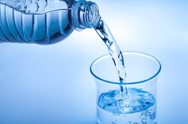 Drink water pouring in to glass over light blue background
