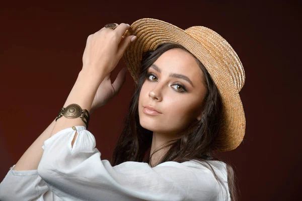 Vacker flicka i en halm hatt poserar i studion på en brun ba — Stockfoto