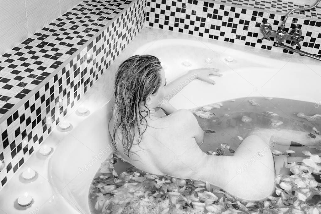 girl lying in bath, rose petals, burning candles. Black and whit