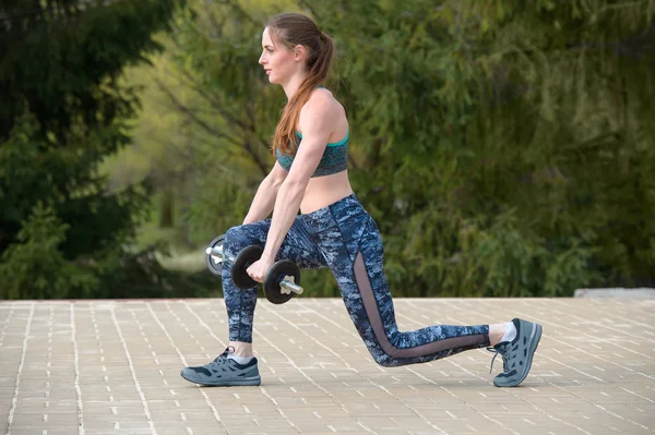 Junge athletische Frau im Trainingsanzug beim Ausfallschritt mit Hanteln — Stockfoto