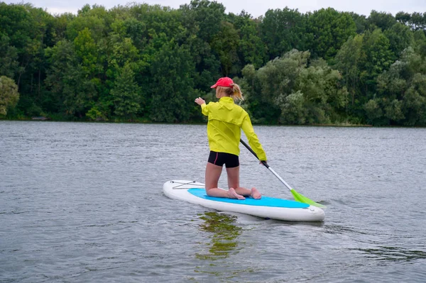 Femme s'agenouille sur une planche de surf et tient une pagaie. Vue arrière — Photo