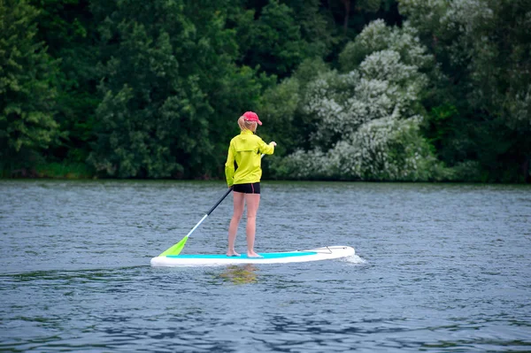 Une jeune femme flotte sur un tableau SUP le long d'une grande rivière. Nage encore. — Photo