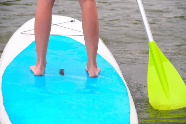 Jambes d'une jeune femme debout sur une planche à pagaie à la surface — Photo