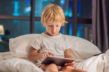 Çocuk tablet yatağında gitmeden önce bir gece şehir bir arka plan üzerinde uyku için kullanır. Çocuk ve teknoloji kavramları