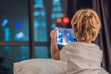 Çocuk tablet yatağında gitmeden önce bir gece şehir bir arka plan üzerinde uyku için kullanır. Çocuk ve teknoloji kavramları