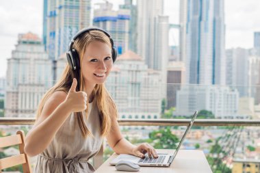 Young woman teaches a foreign language or learns a foreign language on the Internet on her balcony against the backdrop of a big city. Online language school lifestyle