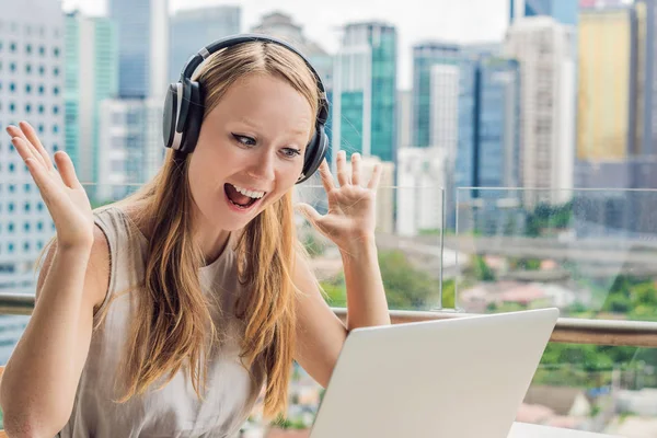 Ung kvinna lär ett främmande språk eller lär sig ett främmande språk på Internet på sin balkong mot bakgrund av en storstad. Online språk skolan livsstil — Stockfoto