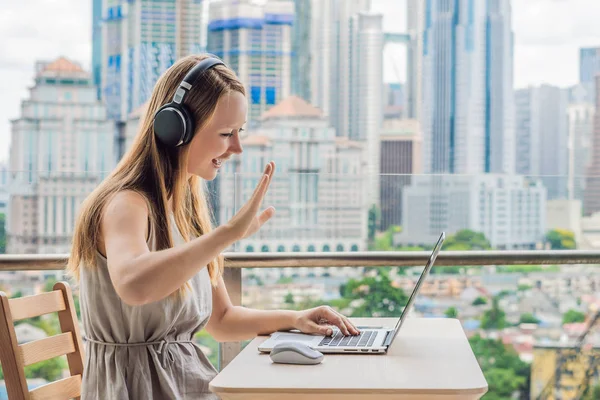 Ung kvinna lär ett främmande språk eller lär sig ett främmande språk på Internet på sin balkong mot bakgrund av en storstad. Online språk skolan livsstil — Stockfoto