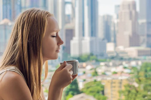 En ung kvinna är att ha frukost på balkongen. Frukostbordet med kaffe frukt och bröd Atlantkusten på en balkong mot bakgrund av den stora staden — Stockfoto