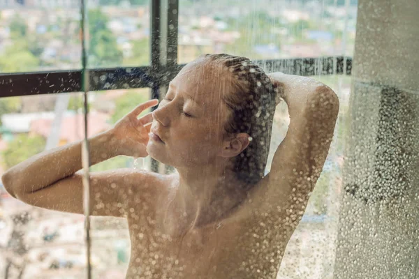 Gündüz, şehrin panoramik manzaralı penceresinin arka plan üzerinde damla ile cam arkasında duşta güzel kadın