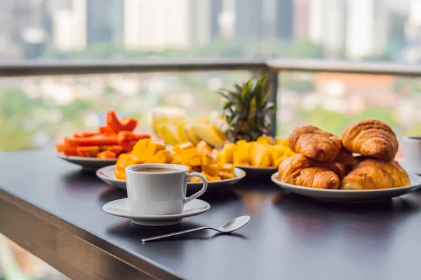 Reggeliző asztal, kávé gyümölcs és kenyeret croisant, egy erkély, a nagy város a háttérben — Stock Fotó