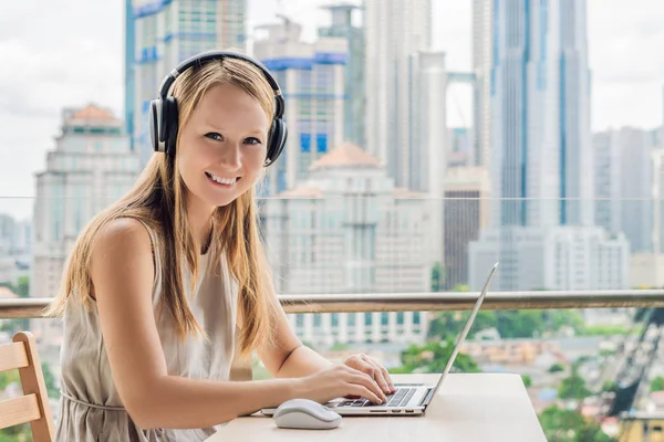 Young woman teaches a foreign language or learns a foreign language on the Internet on her balcony against the backdrop of a big city. Online language school lifestyle.