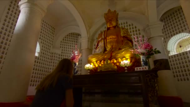 Vrouw bidden tot een gouden Boeddhabeeld binnenkant van de Kek Lok Si tempel op Penang island, Maleisië — Stockvideo