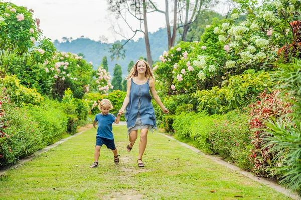 Anne ve oğlu çiçek açan bahçede koşturup. Mutlu aile yaşam tarzı kavramı.