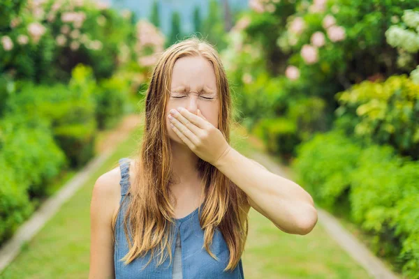 花盛りの木の背景と公園で若い女性のくしゃみ アレルギー花粉コンセプト — ストック写真