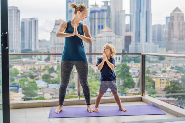 Anne ve oğlu büyük bir şehir arka planda balkonda yoga uygulamak. Spor anne çocukla sabah egzersiz evde yapıyor. Anne ve çocuk çalışmaları birlikte, sağlıklı aile yaşam konsepti yapmak.