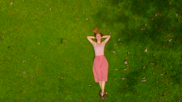 Aerial slowmotion shot of a woman laing on a green lawn. camera raises up — Stock Video