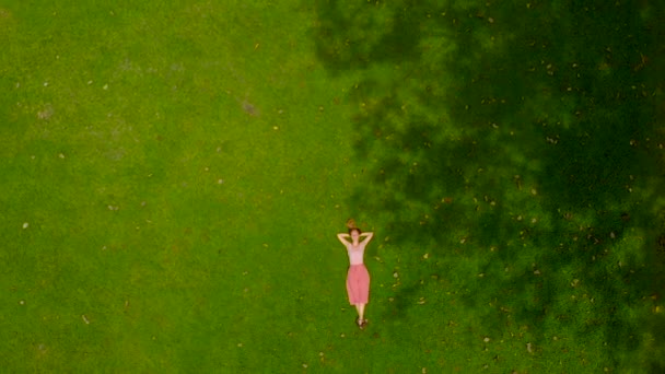 Aerial slowmotion shot of a woman laing on a green lawn. camera raises up — Stock Video