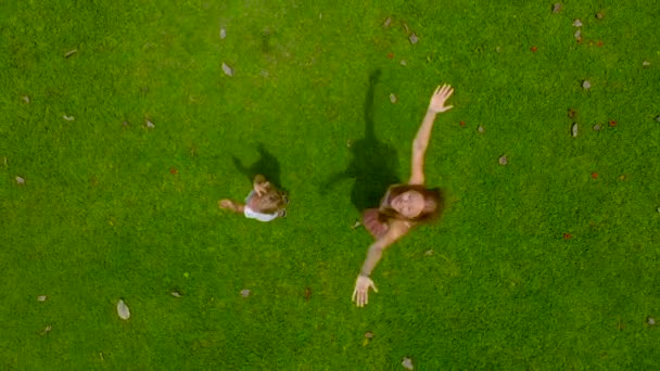 Aerial slowmotion skott av en kvinna och hennes son som snurrar på en grön gräsmatta som tittar på en kamera. kameran höjer upp — Stockvideo