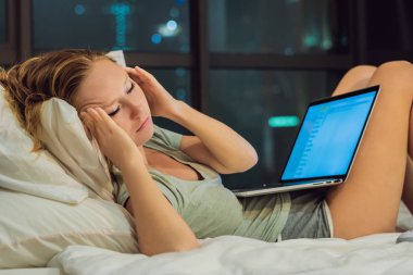 Genç güzel kırmızı saçlı kadın çalışma sıkılmış, uykusuz ve yorgun onun laptop büyük şehir manzaralı penceresinin arka plan üzerinde karanlık odada gece geç saatte yatakta