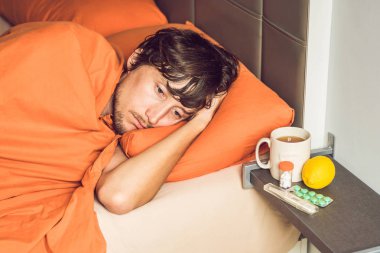 Yatakta yatarken, çay içme ve sıcaklık termometre ile ölçme duygu soğuk, genç adam