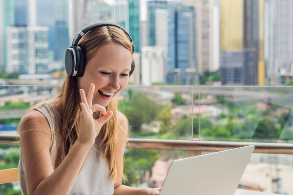 Young woman teaches a foreign language or learns a foreign language on the Internet on her balcony against the backdrop of a big city. Online language school lifestyle.