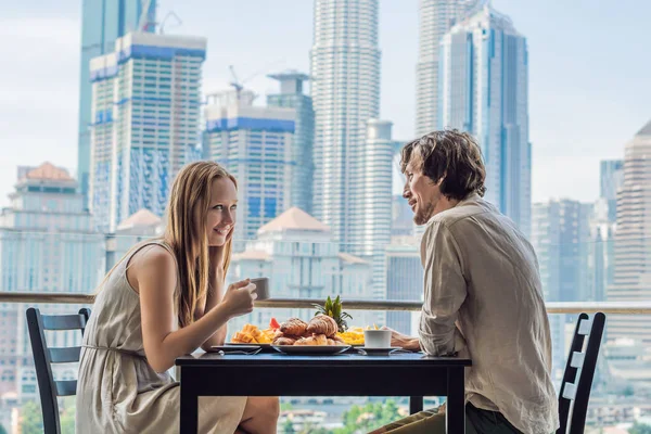 Loving couple having breakfast on the balcony. Breakfast table with coffee fruit and bread croissant on a balcony against the backdrop of the big city.