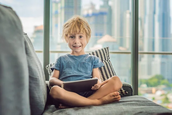 Boy Využívá Tabletu Doma Gauči Pozadí Okna Mrakodrapy Moderní Děti — Stock fotografie