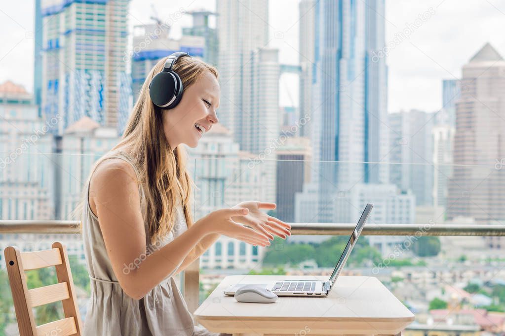 Young woman teaches a foreign language or learns a foreign language on the Internet on her balcony against the backdrop of a big city. Online language school lifestyle.