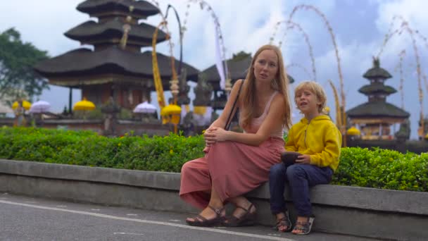 Ung kvinna och hennes son som sitter framför en Pura Ulun Danu tempel på den sjön Bratan i Bali, Indonesien — Stockvideo