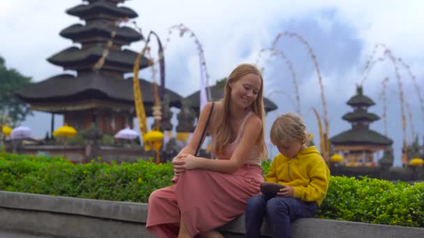 Joven mujer y su hijo sentados frente a un templo Pura Ulun Danu en el lago Bratan en Bali, Indonesia — Vídeos de Stock