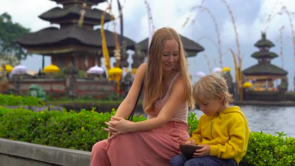 Joven mujer y su hijo sentados frente a un templo Pura Ulun Danu en el lago Bratan en Bali, Indonesia — Vídeos de Stock