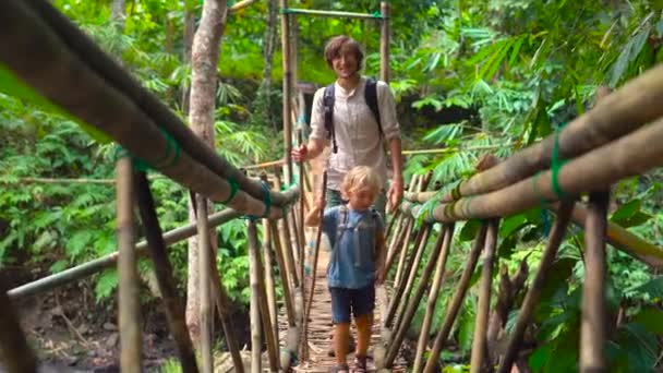 Ojciec som przekraczania tropikalnych rzeki mostem wykonana z bambusa — Wideo stockowe