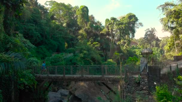Bali, Indonesia - May 15, 2018: aerial shot of a small bridge over the river with a small local temple on it in Bali, Indonesia. Girl in a school dress crossing the bridge — Stock Video