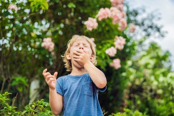 小男孩在公园里打喷嚏 对着一棵开花的树的背景 花粉过敏概念 — 图库照片