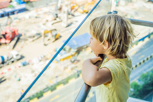 Boy is looking at the construction site. Chooses his future profession.