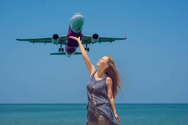 Young woman on the beach and landing plane. Travel concept.