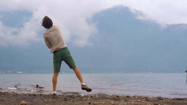 Strzał slowmotion ojca i syna, rzucanie kamieniami w jezioro Bratan w highlands, na wyspie Bali, Indonezja — Wideo stockowe