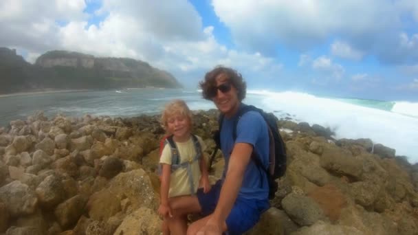 Tikje schot van vader en zijn zonde het maken van een selfie video op een strand met grote golven Melasti strand op het eiland Bali, Indonesië — Stockvideo