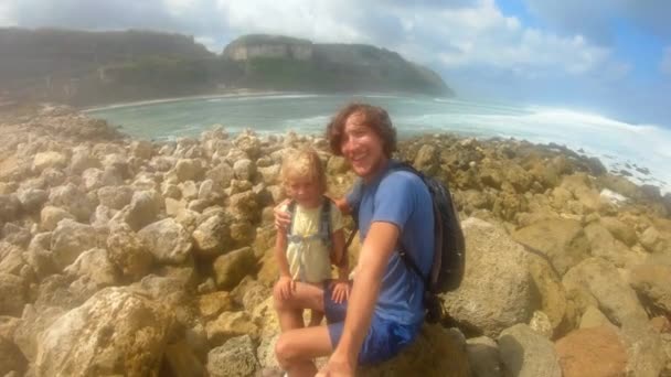 Slowmotion постріл з батьком і його гріх, роблячи це selfie відео на пляжі з великі хвилі Melasti пляж на острові Балі, Індонезія — стокове відео