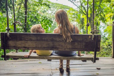 Anne ve oğlu gündüz tropikal bahçe salıncak üzerinde oturan